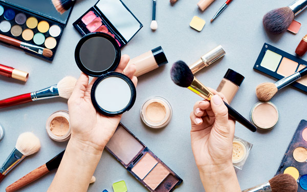机の上に化粧品がならび、中央にブラシとパウダーを持つ手元が見える写真 (c) pressmaster - Fotolia.com