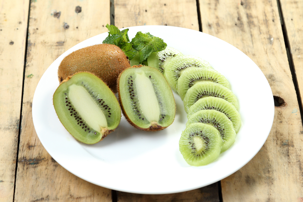 Close up kiwi fruit slice on white dish, Plank wood background.