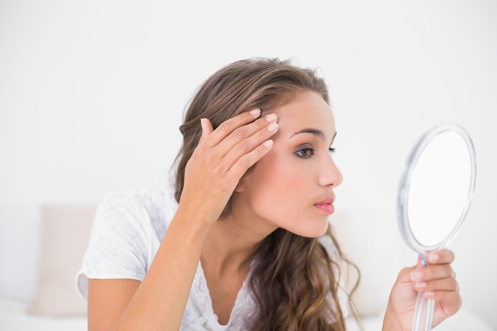 Serious attractive brunette looking at mirror in bright bedroom