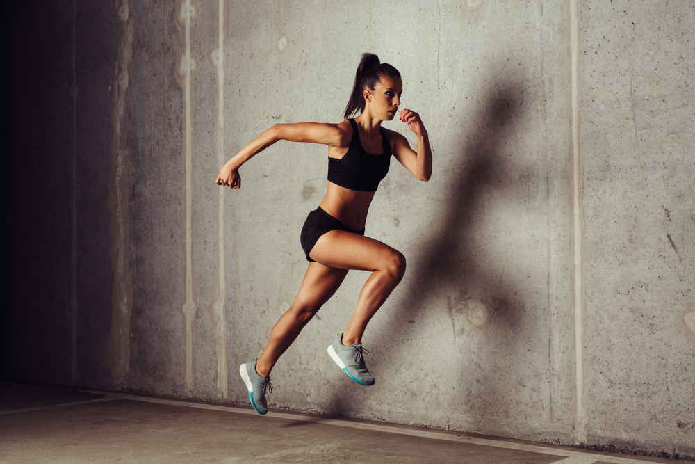 Slim attractive sportswoman running  against a concrete background