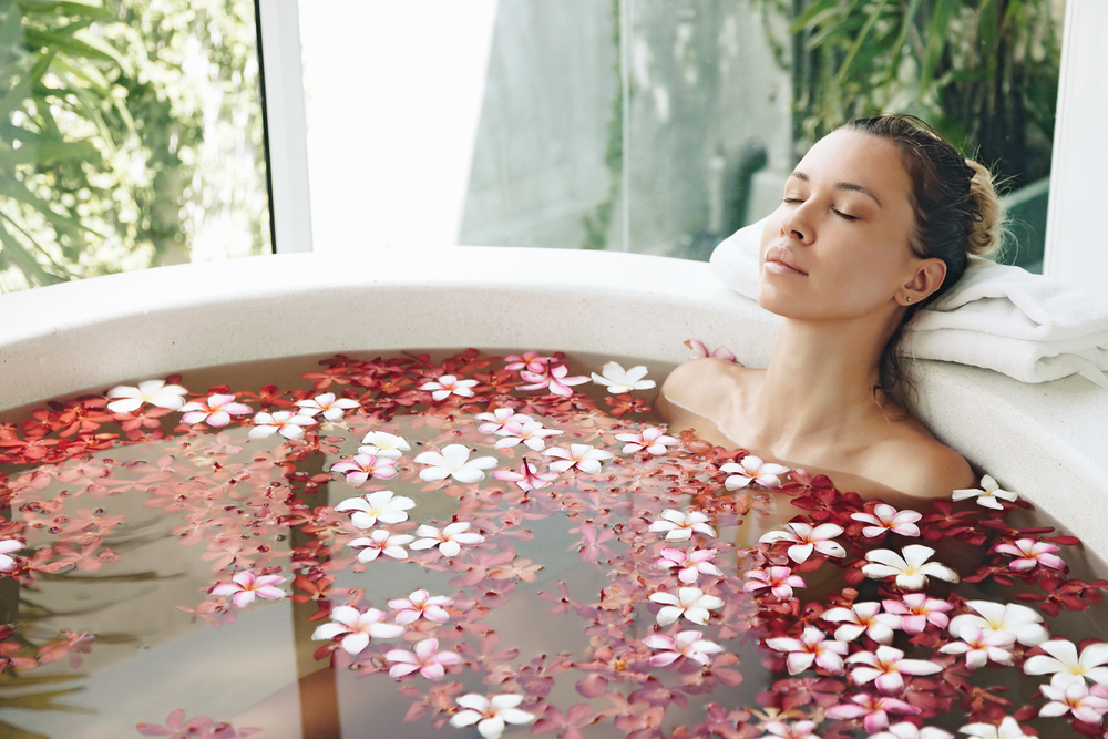 Woman relaxing in round outdoor bath with tropical flowers, organic skin care, luxury spa hotel, lifestyle photo