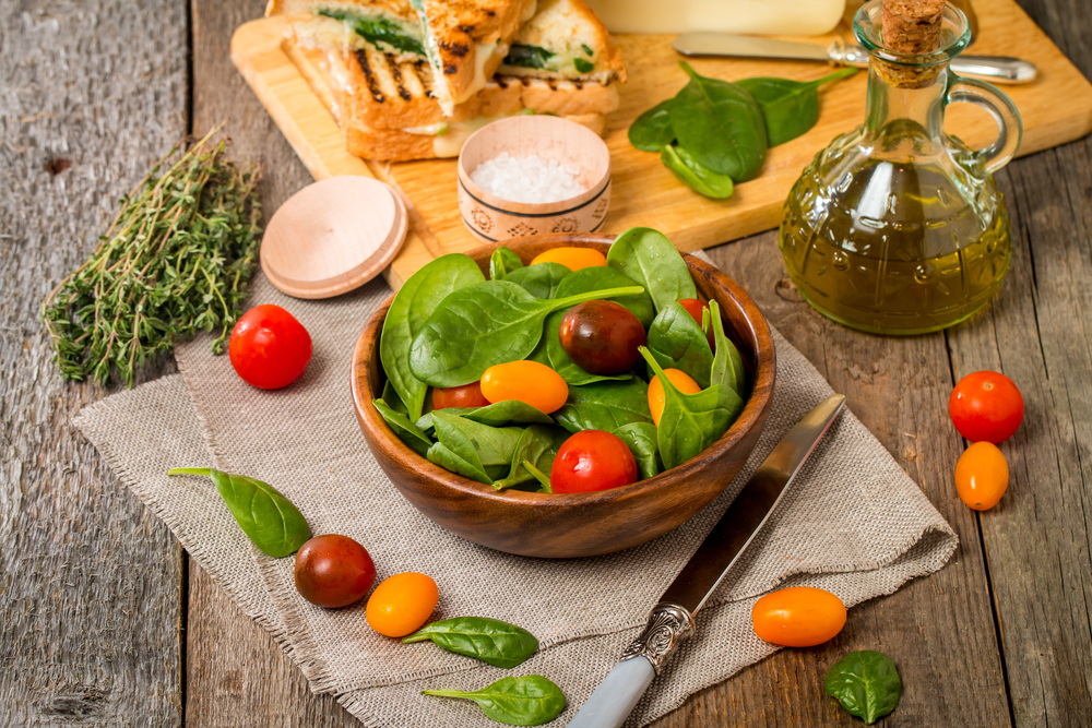 Salad made with baby spinach and cherry tomatoes in a wooden bowl with ingredients.