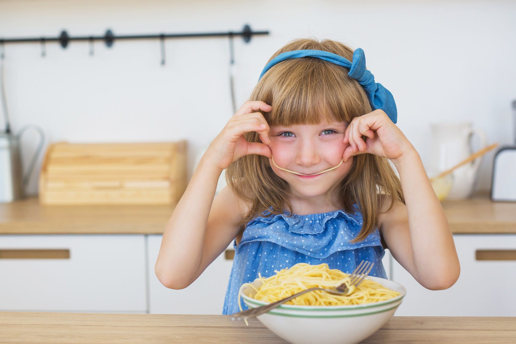 Portrait of a little girl funny eats a spaghetti from a dish and smiling