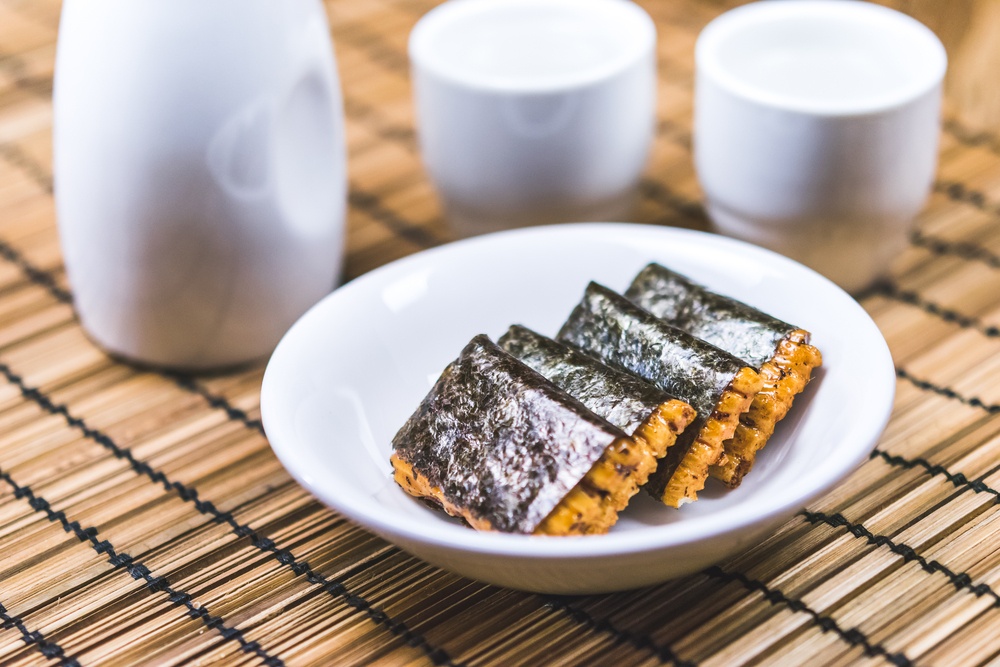 a set of japan rice cracker rolled with seaweed and  tradition Sake on white  bottle on bamboo mat  background.