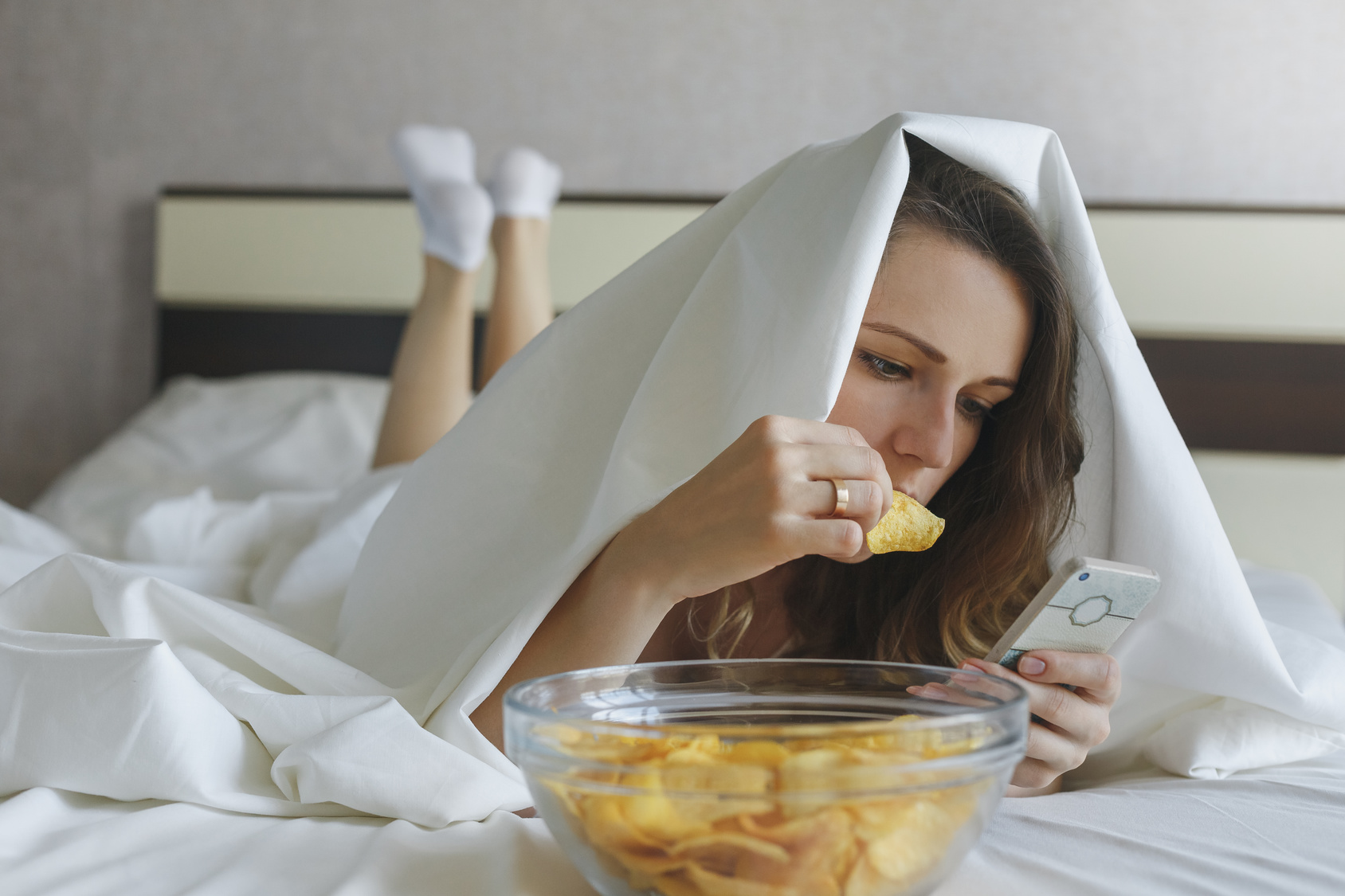 Girl eating chips in bed and watching news in phone