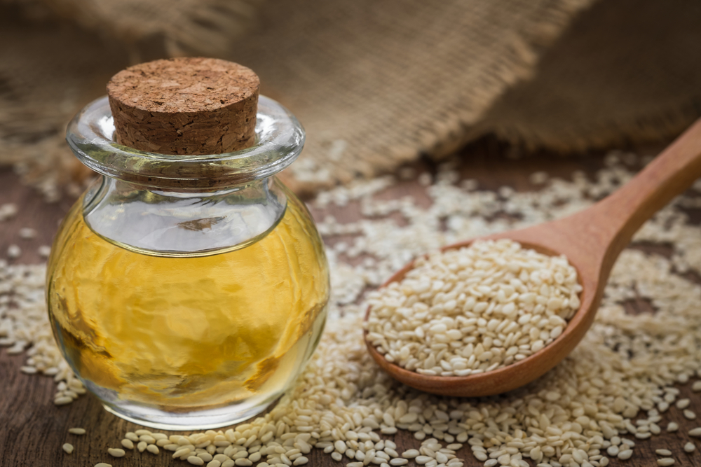 Sesame oil in glass jar and sesame seeds on wooden spoon