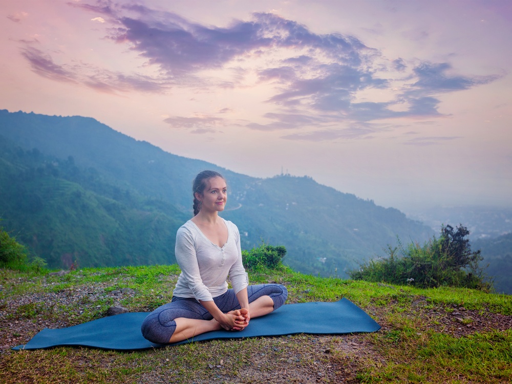 Healthy life exercise concept - Sporty fit woman practices yoga asana Baddha Konasana - bound angle pose outdoors in HImalayas mountains on sunset. Himachal Pradesh, India