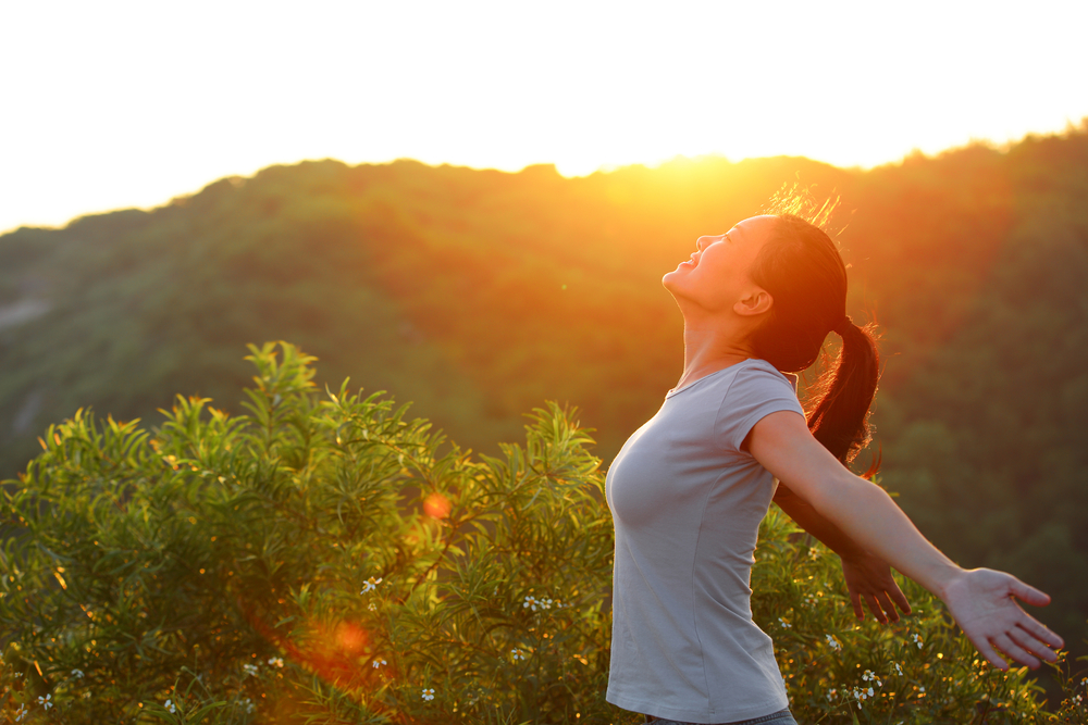 cheering woman open arms at sunrise mountain peak