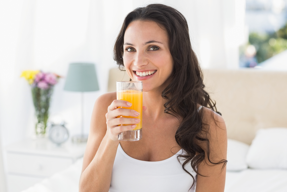 Happy brunette having glass of orange at home in bedroom