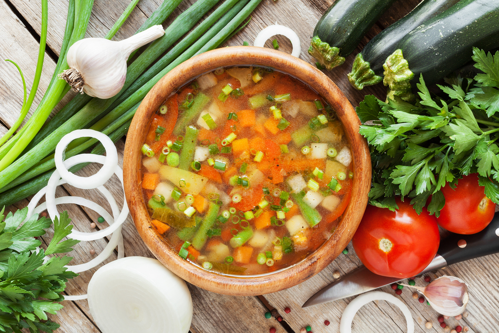 vegetable soup in wooden bowl and ingredients on wooden rustic table. top view